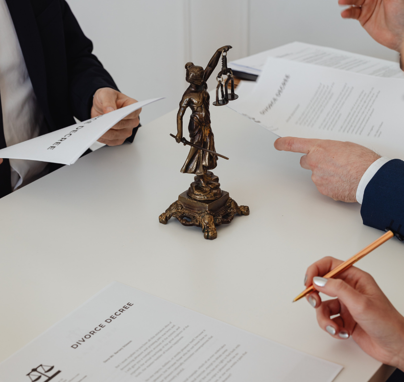 Trzy osoby analizujące dokumenty prawne przy figurce Temidy symbolizujące doradztwo prawne.