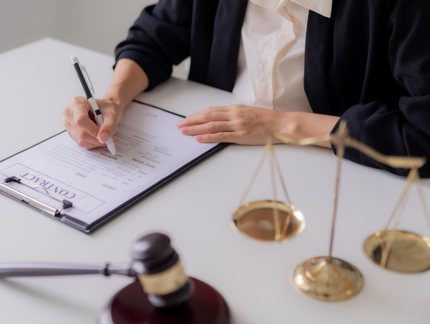 Podpisywanie umowy przez prawnika z wagą Temidy i młotkiem sędziowskim na biurku.